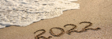 2022 written in the sand with a wave coming in