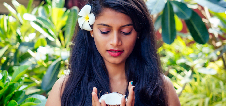 indian woman with a white flower in hear hair holding an open coconut