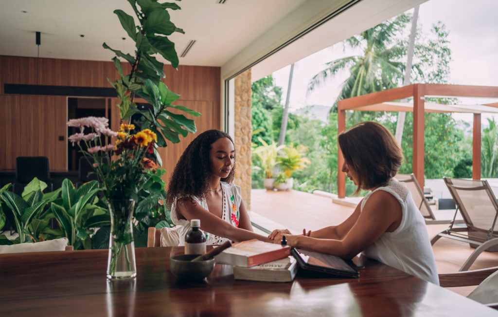 An ayurvedic therapist is checking the pulse of young woman during consultation at home.