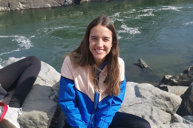 Photo of Amalia Arango smiling sitting on a rock next to a light blue river