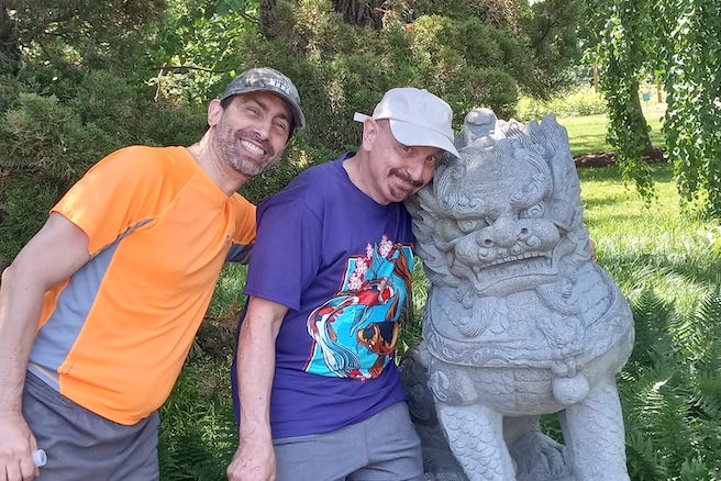 A photo of Andy, a panchakarma bodywork technician, with his husband next to a dragon statue